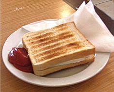 a grilled cheese sandwich with ketchup on a white plate sitting on a wooden table