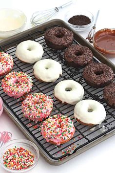 doughnuts on a cooling rack with frosting and sprinkles in bowls