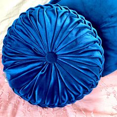 two blue round pillows sitting on top of a pink bed sheet with white sheets behind them