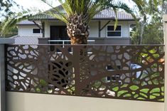 a house with a palm tree in the foreground and a metal fence behind it