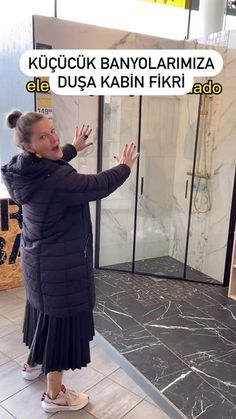 a woman in a black coat and white shoes standing next to a glass shower door