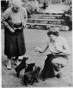 an old black and white photo of two women playing with puppies in the yard