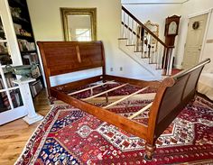 a wooden bed frame sitting on top of a rug in a living room next to a stair case