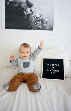 a baby sitting on top of a bed next to a black and white sign that says b months, b months, b months out