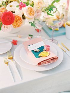 the table is set with white plates, silverware and colorful flowers in vases