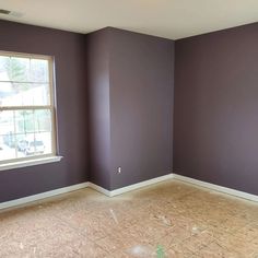 an empty room with purple walls and white trim on the windowsill, in front of a large window