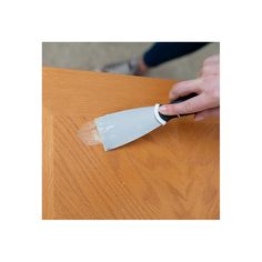 a person using a knife to paint a wooden table with white adhesivement on it