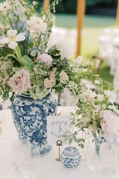 an arrangement of flowers in blue and white vases sitting on a table with glasses