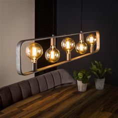 an industrial style light fixture hanging over a wooden table with potted plants on it