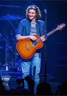 a man standing in front of a microphone holding a guitar