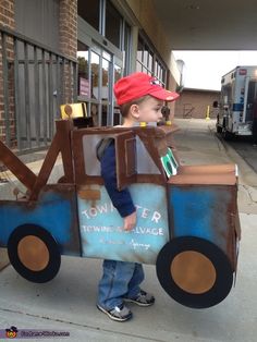 a young boy dressed up as a tow truck and holding a cardboard sign that says tower