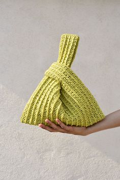 a hand holding a yellow knitted bag in front of a white wall and floor