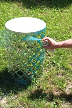 someone is spraying something on top of a trash can in the grass with a spray bottle