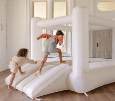 two children are playing in an inflatable play area with white walls and wood floors