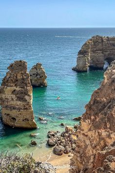 two large rocks sticking out of the ocean next to a beach with people swimming in it