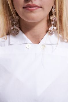 a woman with blonde hair wearing large earrings and a white shirt is looking at the camera