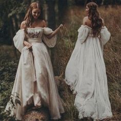 two women in white dresses standing next to each other on the grass with trees in the background