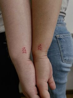 two people holding hands with tattoos on their arms and the word love written in red ink