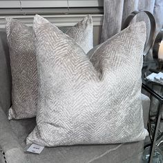 two gray pillows sitting on top of a couch next to a glass table with a candle