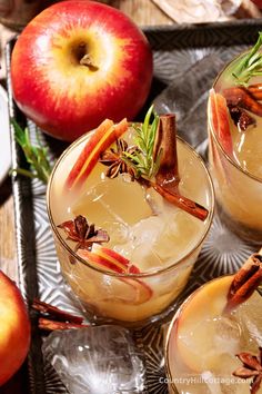 three glasses filled with apple cider and cinnamon stick garnish on a tray