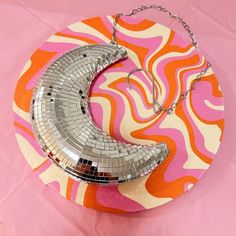 a silver crescent shaped mirror necklace on a pink and orange plate with chains hanging from it