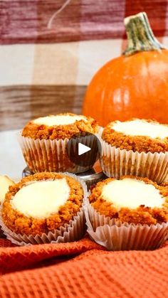 cupcakes with icing sitting on top of an orange cloth next to a pumpkin