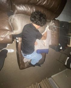 a young man sitting on top of a brown leather couch next to a white dog