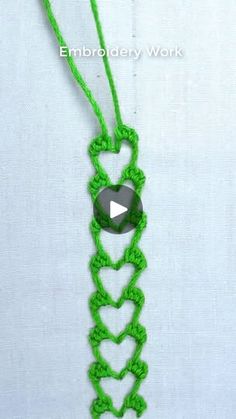 a green crochet necklace with a black button on the end and an arrow in the middle