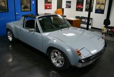 a blue sports car parked in a garage next to a wall with posters on it