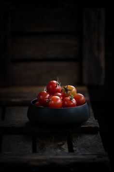 a bowl filled with lots of tomatoes on top of a wooden table in the dark