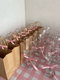 many wine glasses are lined up on a table with pink bows and brown paper bags