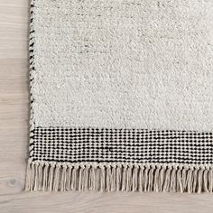 a black and white rug with fringes on top of a wooden floor next to a wall