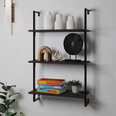 three shelves with books and vases on them against a wall next to a potted plant