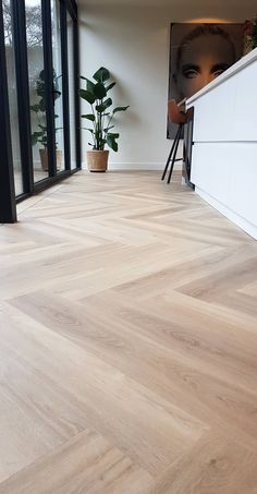 an empty room with wood flooring and plants in the window sill, next to a large painting on the wall