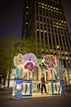 a man standing in front of a building decorated with lights and flowers on display at night