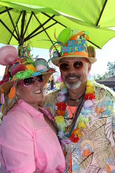 a man and woman are standing under an umbrella at a beach party wearing colorful hats