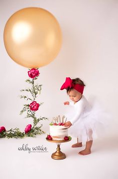 a baby girl standing in front of a cake with a balloon above her head and holding onto it