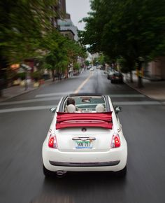 a white car driving down a street next to tall buildings with trees on both sides