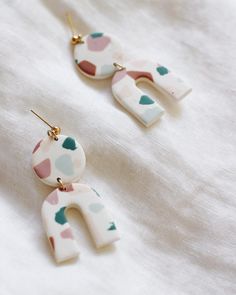 two pairs of white and pink earrings with hearts painted on them sitting on top of a white sheet