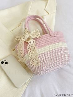 a pink and white purse sitting on top of a bed next to a cell phone