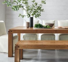 a wooden table with white chairs and a bowl of vegetables on the table next to it