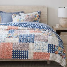 a bed with a blue and orange quilt on it's cover, next to a night stand