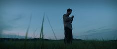 a man standing in tall grass looking at his cell phone