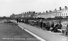 an old black and white photo of people sitting on park benches in front of houses