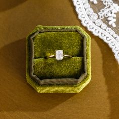 an engagement ring sits in a green velvet box