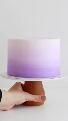 a hand is holding a cake on a white plate with purple ombretta frosting