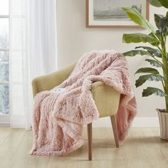 a chair with a pink blanket on it next to a potted plant and window