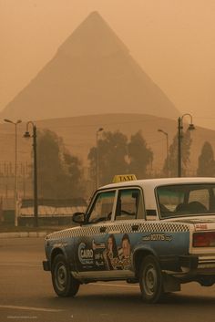 a taxi cab driving down a street next to a tall pyramid in the distance,