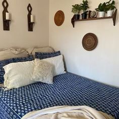 a bed with blue and white bedspread next to two potted plants on the wall