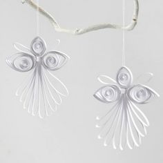 two ornaments hanging from a tree branch on a white background, one is shaped like an angel and the other has wings